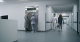 Nurse with old patient wait for elevator in medical center hallway. African American doctor walks down corridor with wheelchair. Caucasian medic goes to his patient. Medical staff at work in clinic.