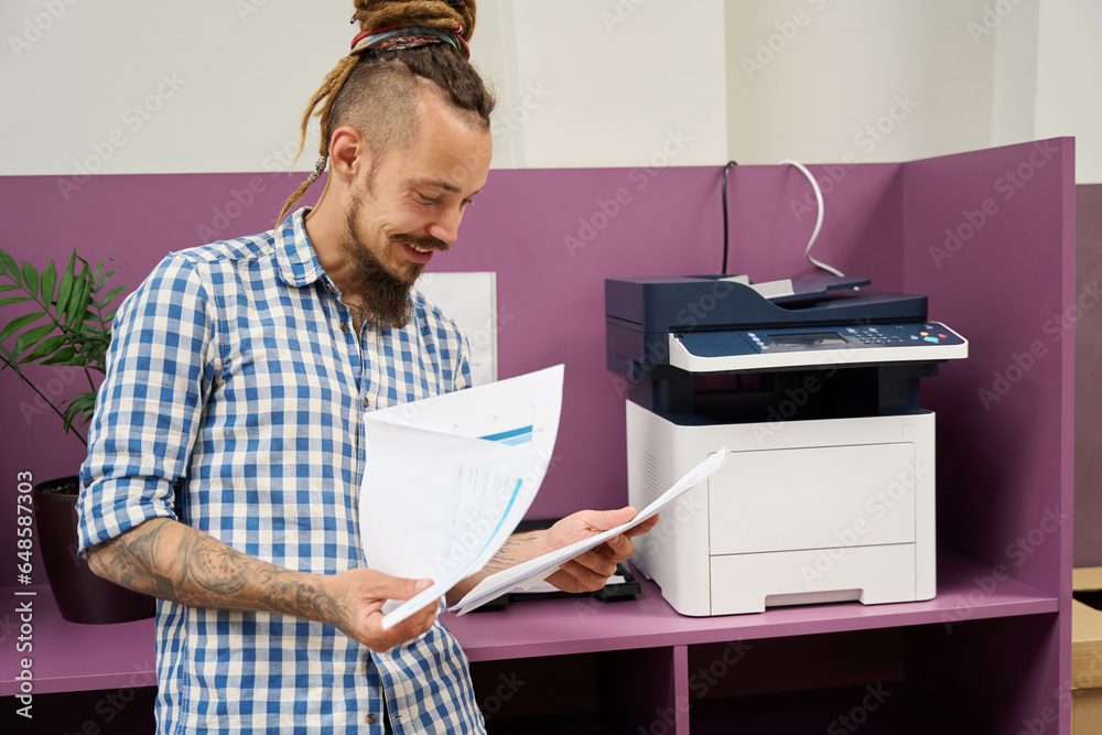 Man with dreadlocks stands near a photocopier in coworking space Man with dreadlocks stands near a photocopier in coworking space