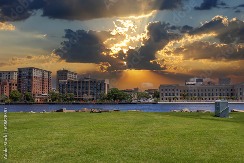A beautiful summer landscape along Cape Fear river with lush green trees and grass, hotels and office buildings along the banks, powerful clouds at sunset at Battleship North Carolina in Wilmington