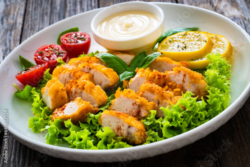 Seared breaded chicken nuggets with mayonnaise and fresh vegetables on wooden table
