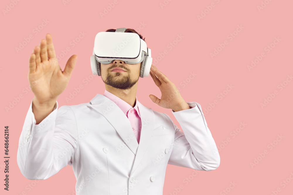 Virtual reality technology. Serious young elegant man touches air during virtual reality isolated on pink background. Male VR user in white formal suit uses modern device in his work. Banner.