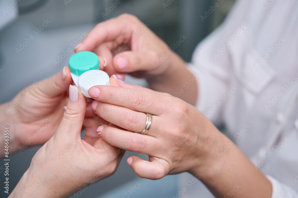 Optician demonstrating plastic container for ophthalmic lenses to client Optician demonstrating plastic container for ophthalmic lenses to client