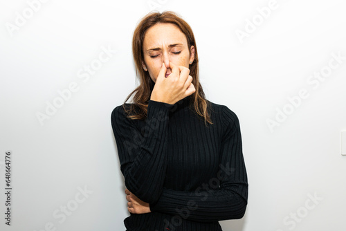 beautiful 40 year old woman holding her nose because of bad smell on white background