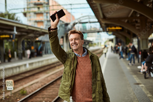 Middle aged businessman going on a business trip and waving at a arrival of his train in a train station