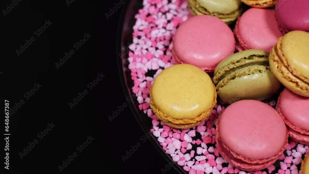 Top view of rotating fresh macaron cookies. Traditional french desserts from almond dough. Colourful sweet macaron cakes rotating against black background with copy space. French sweets concept. Top view of rotating fresh macaron cookies. Traditional french desserts from almond dough. Colourful sweet macaron cakes rotating against black background with copy space. French sweets concept.