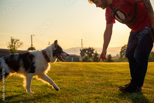 Photography young man teaching his border collie dog the command come here at sunset in a field