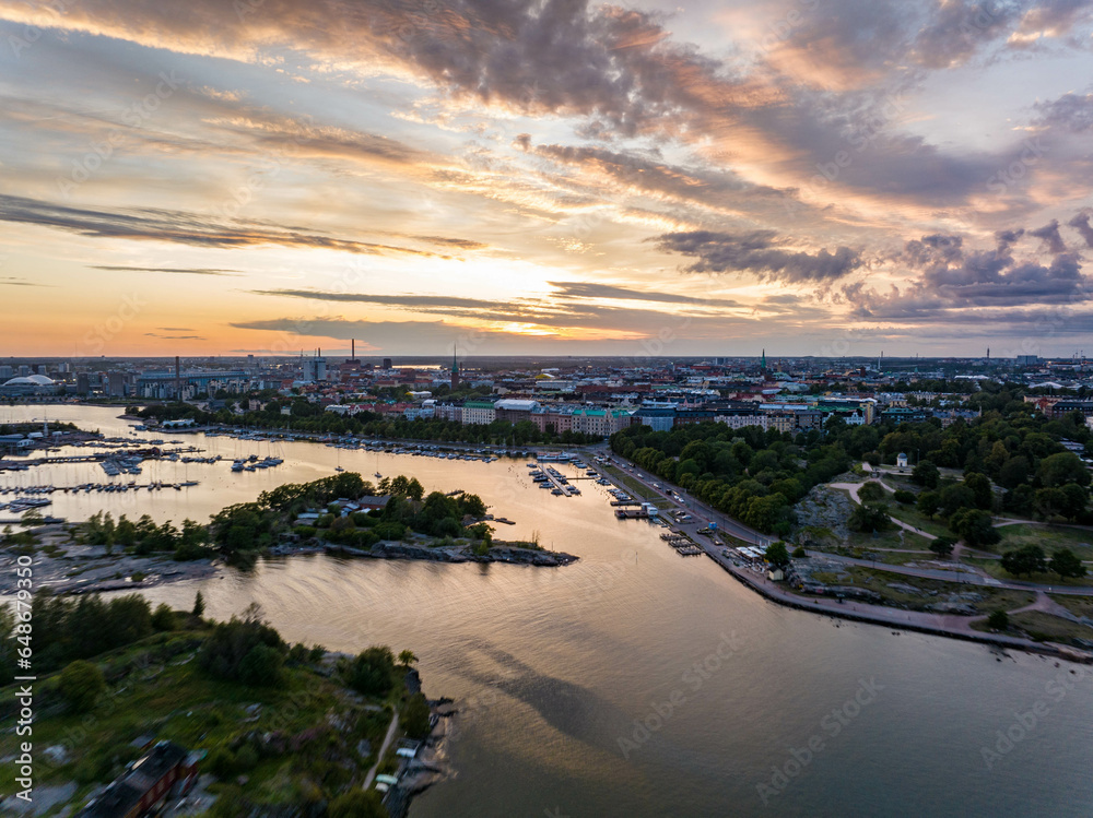 Aerial view of boats in harbour and multistorey apartment buildings in residential urban neighbourhood. Reflection of colourful romantic sunset sky on water surface. Helsinki, Finland