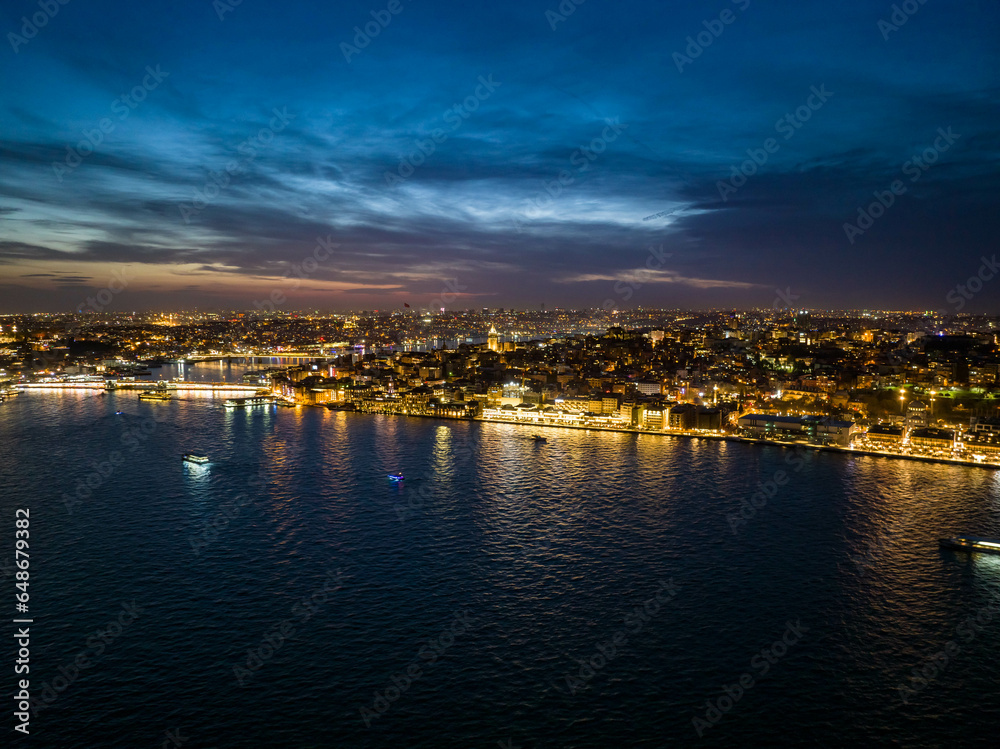 Amazing evening shot of illuminated streets and buildings in city. Boats on water surface around. Night life in metropolis. Istanbul, Turkey
