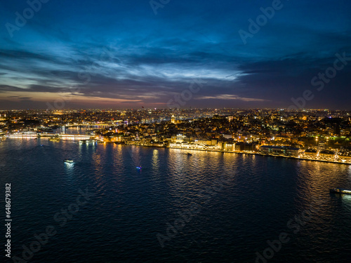 Amazing evening shot of illuminated streets and buildings in city. Boats on water surface around. Night life in metropolis. Istanbul, Turkey