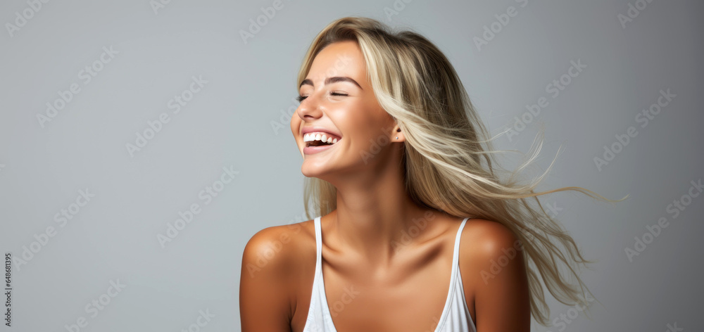 laughing young blonde woman with good skin and teeth on neutral gray background with copy space