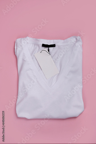top view of white V-neck t-shirt folded with label on pink background