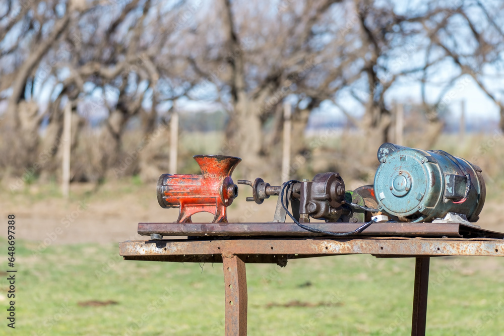 Old manual meat grinder converted to electric in an unsafe manner and mounted on a rustic cart Old manual meat grinder converted to electric in an unsafe manner and mounted on a rustic cart