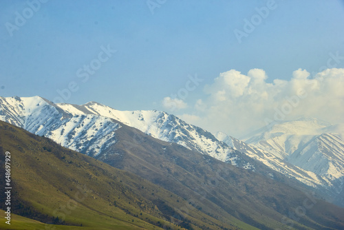 landscape against a mountain backdrop of high mountain ranges with snow-capped mountains and a blue sky with clouds