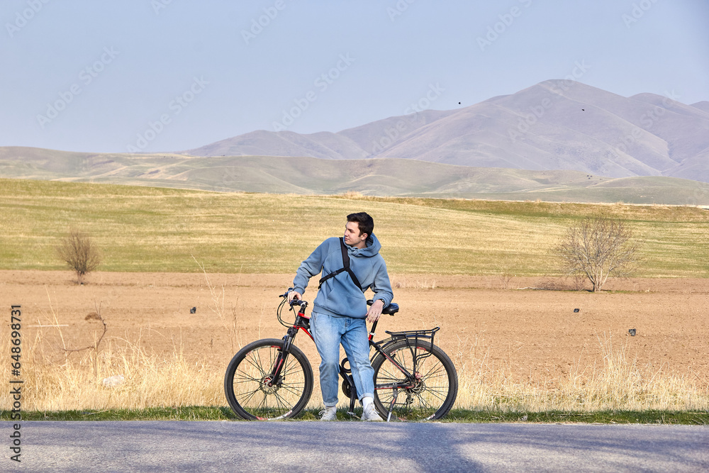 A teenage tourist with a bicycle on the background of the highlands in the fresh air