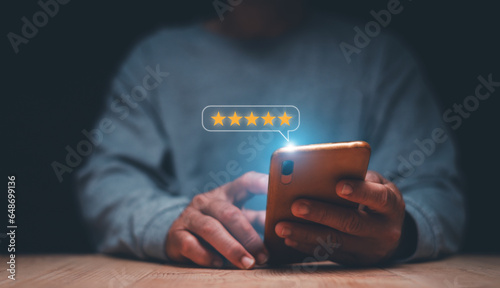 Businessman using smartphone to give five-star symbol for highest satisfaction, 5-star feedback, reputation and quality Concept of standardization and quality in products and services.