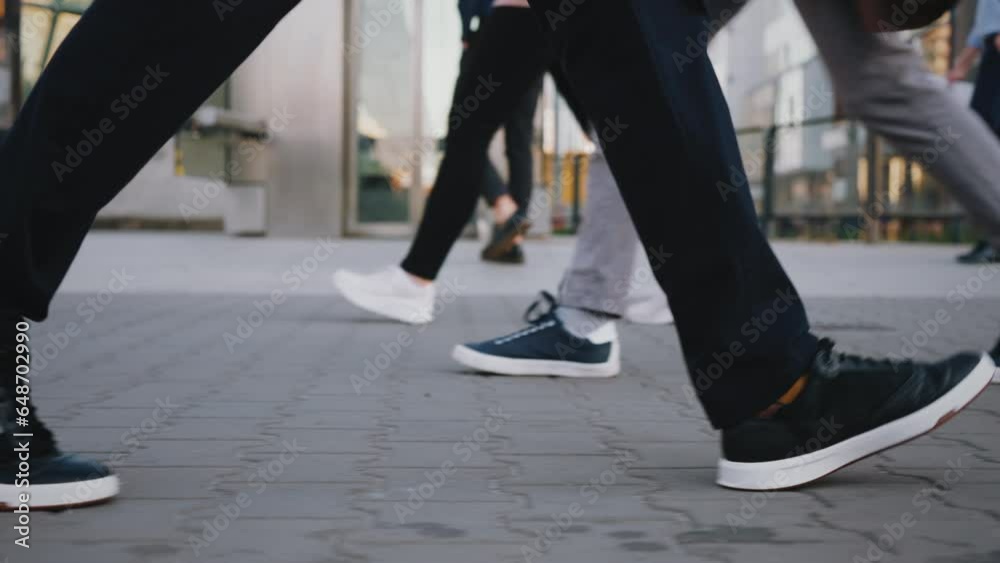 Side view following male feet crossing busy street. Man wearing casual dark trousers leather sneakers goes on pedestrian crossing in big city. Low angle people crowd legs walking urban sidewalk Side view following male feet crossing busy street. Man wearing casual dark trousers leather sneakers goes on pedestrian crossing in big city. Low angle people crowd legs walking urban sidewalk
