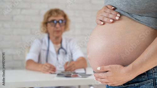 Doctor obstetrician gynecologist at his desk in the background. Close-up of a pregnant woman's belly. photo