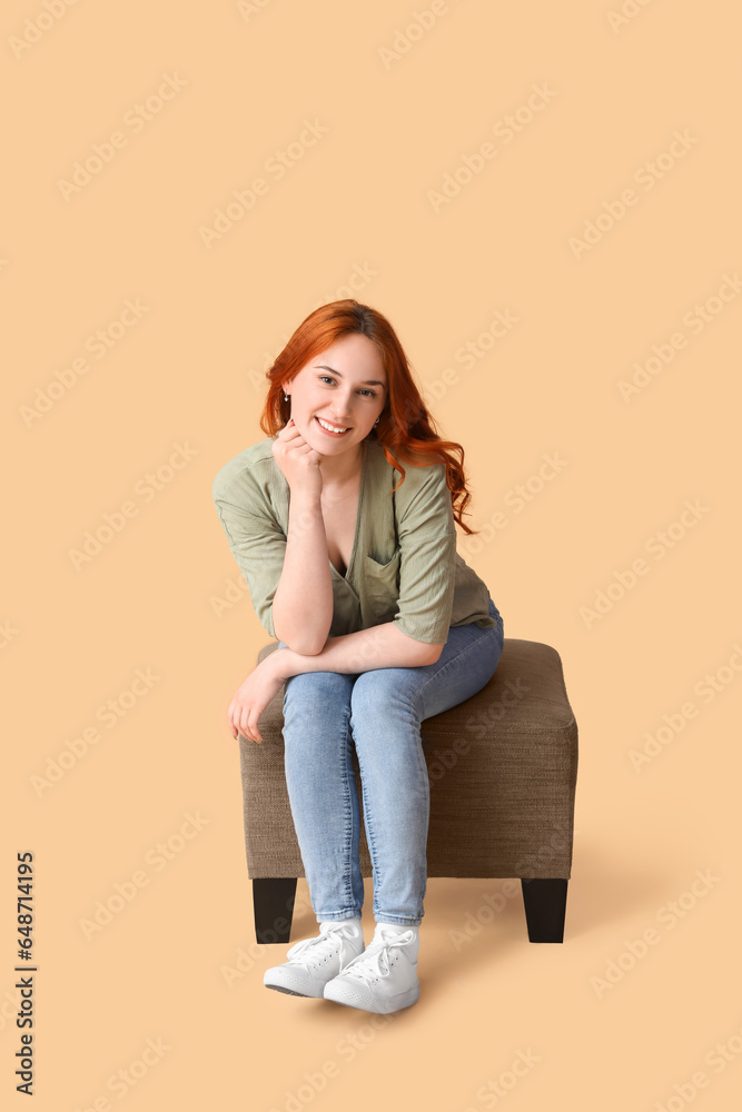Young woman sitting on pouf against beige background Young woman sitting on pouf against beige background