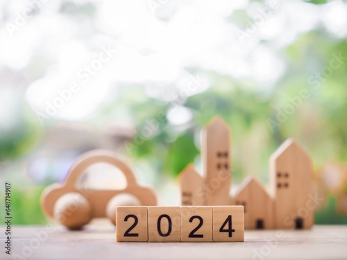 Close up of wooden block number 2024 with miniature house and toy car background. The concept of Transportation insurance, Property investment, House mortgage, Real estste in new year 2024