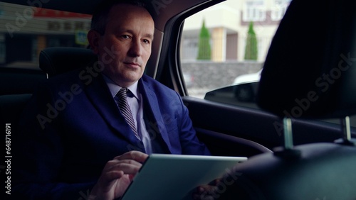 Serious businessman uses computer tablet to obtain business information in interior of business car. Business man works in car. Politician works and looks at information on tablet in car. Man in suit © zoteva87