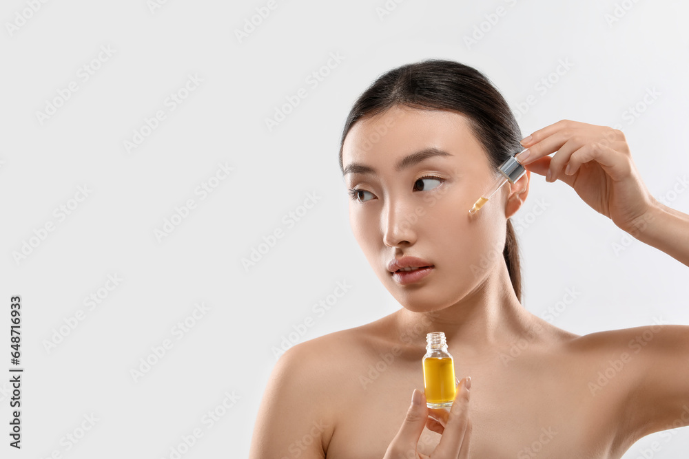 Fototapeta premium Beautiful young woman applying cosmetic serum onto her face on white background, space for text