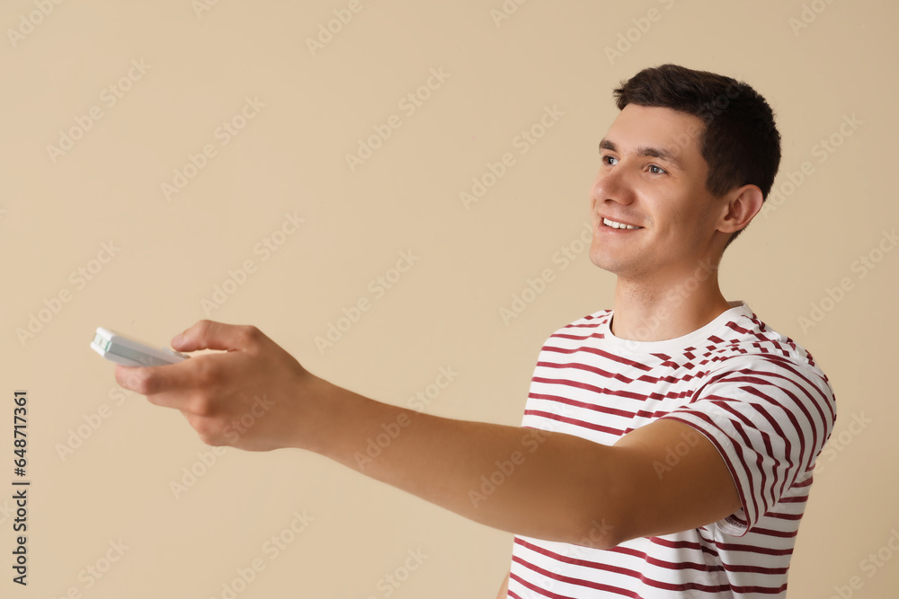 Young man with air conditioner remote control on beige background Young man with air conditioner remote control on beige background