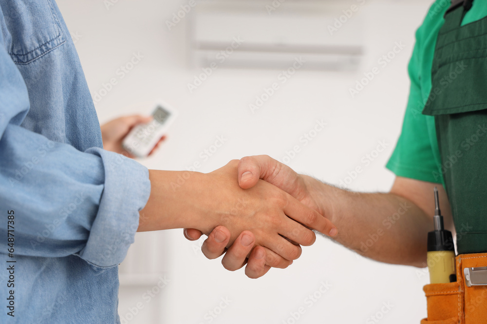 Young man with air conditioner remote control and technician shaking hands at home, closeup Young man with air conditioner remote control and technician shaking hands at home, closeup