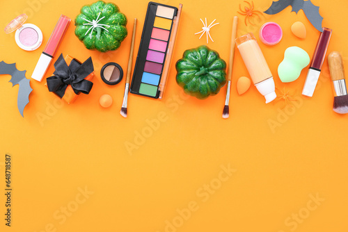 Makeup products and Halloween decor on orange background