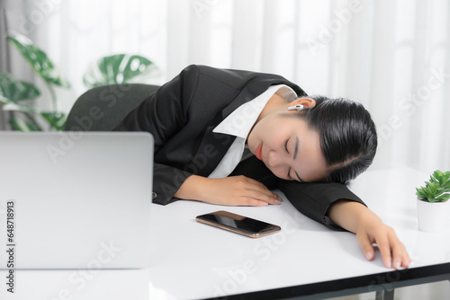 Sleepy and tired young Asian businesswoman or female offie worker taking nap or sleep on her office desk. photo