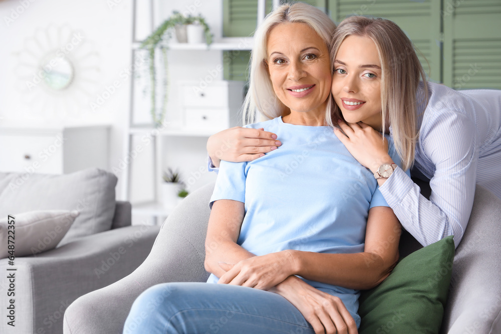 Happy young beautiful woman with her mother sitting on armchair in living room Happy young beautiful woman with her mother sitting on armchair in living room