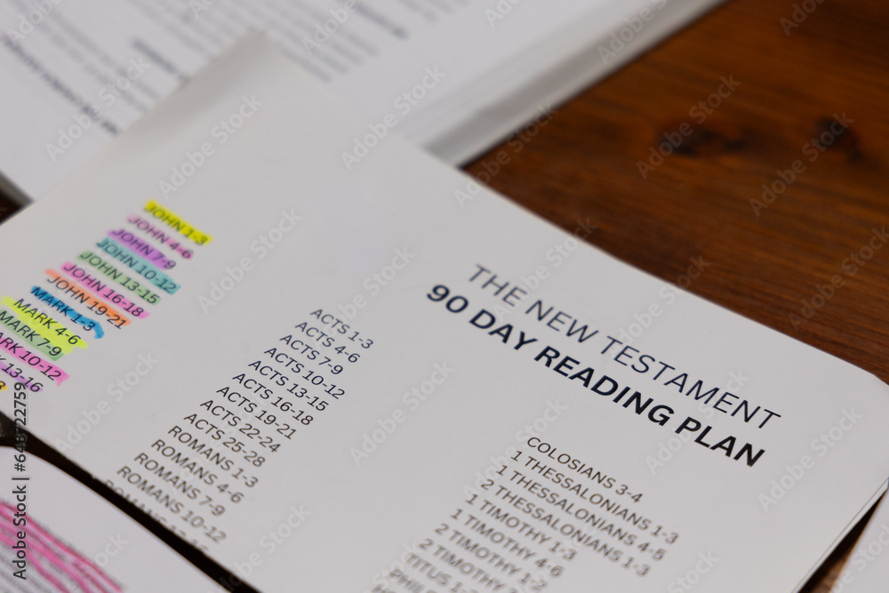 Close up of New Testament 90-Day Reading Plan sheet on wooden table next to study booklet for Bible study Close up of New Testament 90-Day Reading Plan sheet on wooden table next to study booklet for Bible study