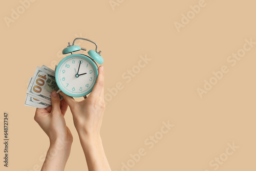 Female hands holding alarm clock and money on beige background
