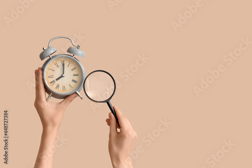Fototapeta Naklejka Na Ścianę i Meble -  Female hands holding alarm clock and magnifier on beige background