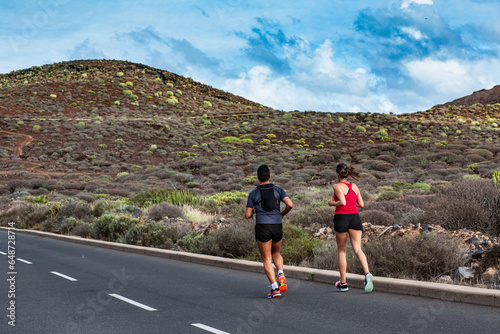 man with woman jogging on a mountain road- A pair of athletes jog along the road in the mountains. A man and a woman train together in the summer to participate in a marathon. Young people working out