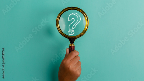 Hand holding a magnifying glass with a question mark icon on the blue background with copy space. Problem solving troubleshooting education concept.