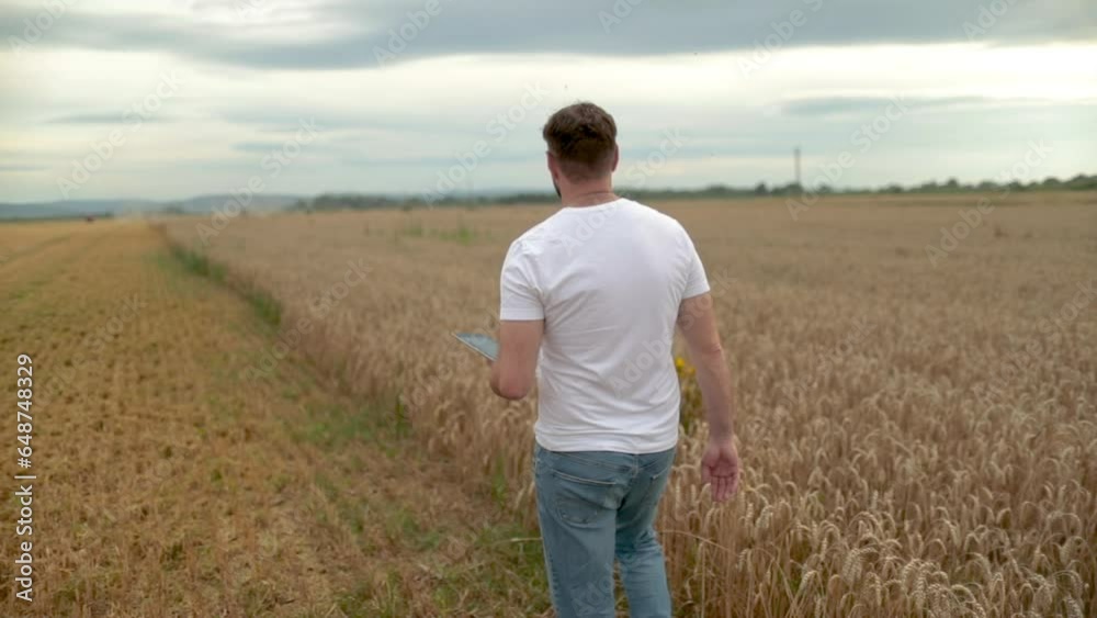 The concept of agriculture. Agronomist in white t-shirt and jeans walking in wheat field. Agricultural technology. A farmer checks the growth of wheat. Organic products. Growing food The concept of agriculture. Agronomist in white t-shirt and jeans walking in wheat field. Agricultural technology. A farmer checks the growth of wheat. Organic products. Growing food