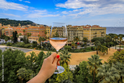 Woman s hand holding a glass of rose provencal wine at an outdoor restaurant with a background of blurred buildings in Old Town Nice, South of France