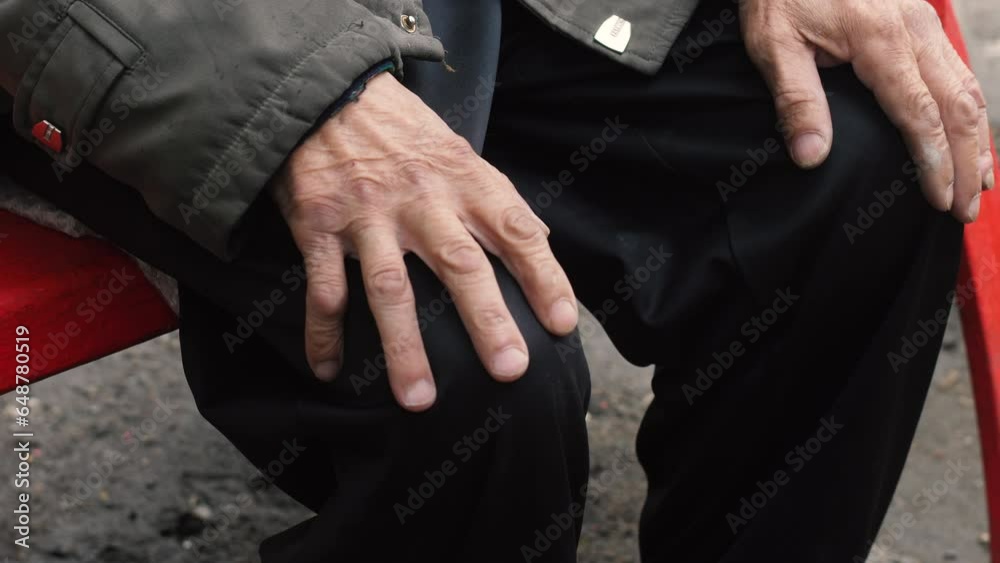 close-up of the hand of an elderly man sitting on a bench alone. a pensioner in the park sits on a bench in the fall. depression, loneliness in older people.
