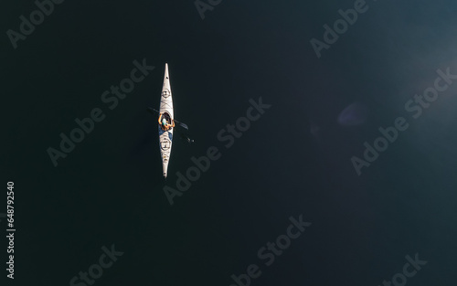 Overhead aerial view of person paddling kayak on dark blue water.