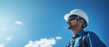 engineer with helmet and safety cloth stands against blue sky