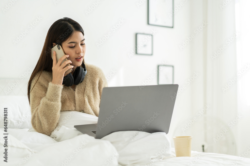 Young smiling happy beautiful asian woman relaxing using laptop computer in the bedroom at home.Young creative girl working and typing on keyboard.work from home concept Young smiling happy beautiful asian woman relaxing using laptop computer in the bedroom at home.Young creative girl working and typing on keyboard.work from home concept