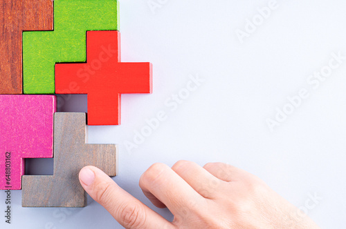 Hand holding wooden puzzle element. Hand sets the last element of the puzzle. The concept of logical thinking. Geometric shapes on a wooden background. Wooden blocks.