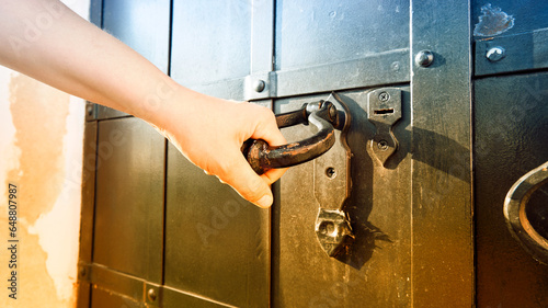 Obraz na plátně A young woman's hand opens an antique metal door. Toned image