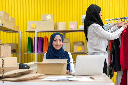 Muslim two asian woman freelancer sme business online shopping working and checklist order with cardboard box on table at home - Business online shipping and delivery concept