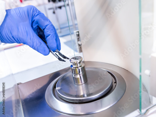 Εκτύπωση καμβά A operator's hand is holding steel calibration weight to place on the analytical balance