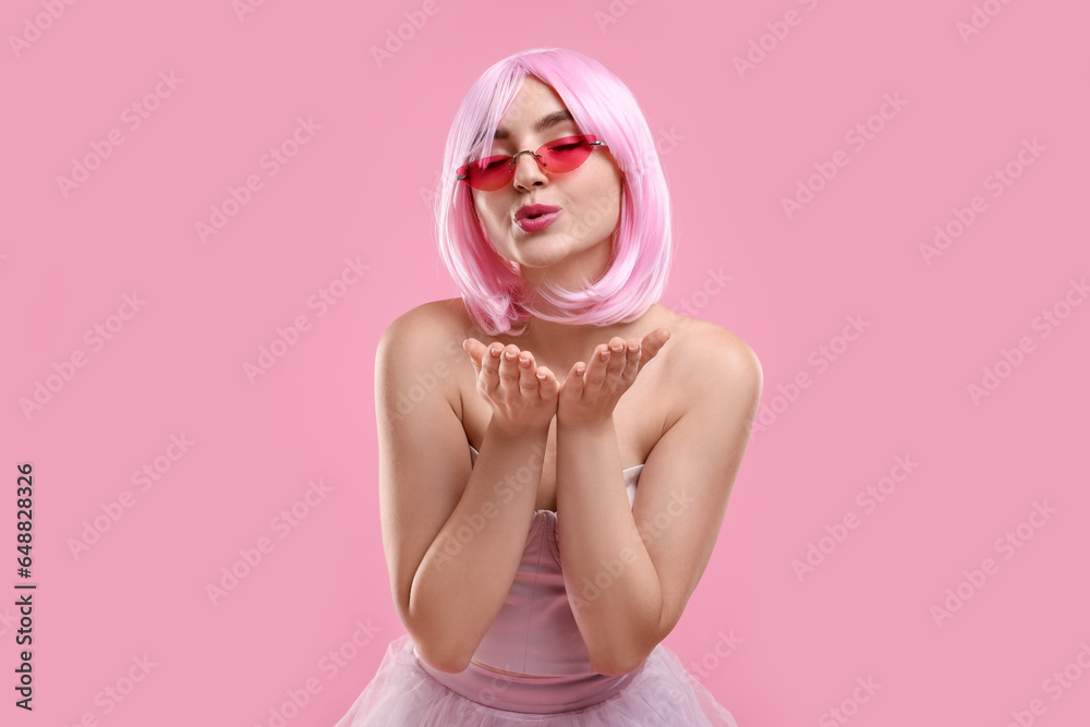 Pink look. Beautiful woman in wig and bright sunglasses blowing kiss on color background