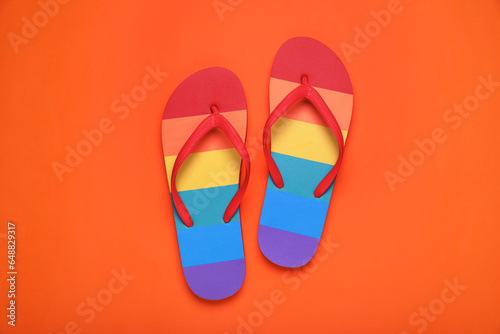 Rainbow flip flops on orange background, flat lay. LGBT pride