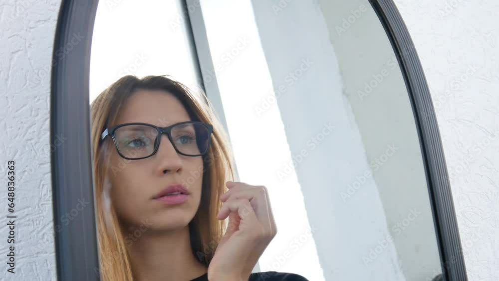 A young pretty woman trying on glasses with black frames in front of a mirror A young pretty woman trying on glasses with black frames in front of a mirror