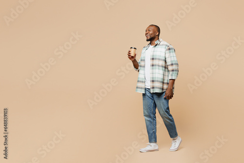 Full body young man of African American ethnicity wear light shirt casual clothes hold takeaway delivery craft paper brown cup coffee to go isolated on plain pastel beige background Lifestyle concept