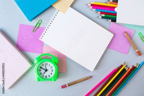 Back to school, alarm clock, colorful sticky notes and colorful pencils, drawing supplies on gray background with copy space, top view, flatly